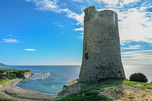 An ancient stone watchtower stands atop a cliff with lush greenery, surveying the rocky coast and rolling waves below