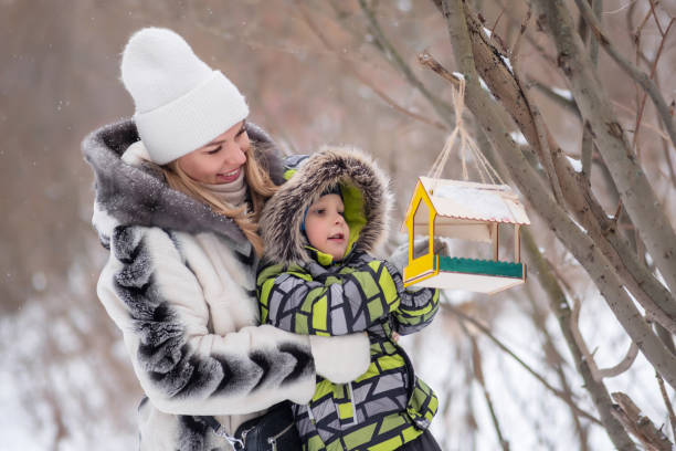 istock mother and son in a winter park feed birds using a feeder 1965395594