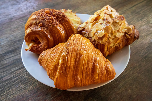 Croissants of various flavors on a white plate on a delicious wooden table, paired with morning coffee.