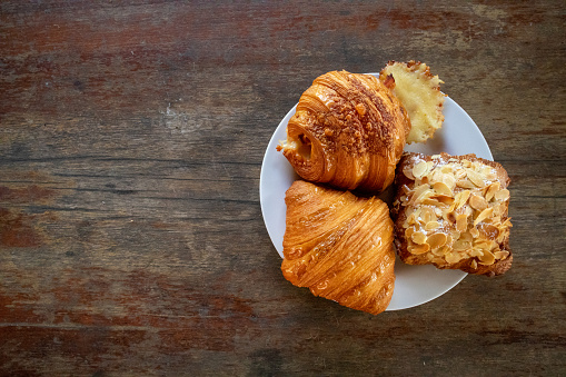 Croissants of various flavors on a white plate on a delicious wooden table, paired with morning coffee.