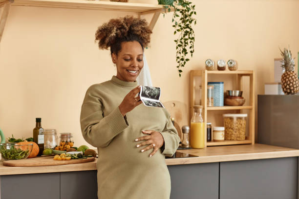 Cheerful Pregnant Woman Looking at Sonogram in Kitchen