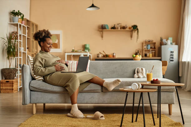 Cheerful Expectant Mother on Cozy Sofa with Laptop
