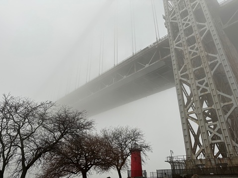 Panoramic view of the George Washington Bridge above the Little Red Lighthouse by the Hudson River surrounded by dense fog on a winter day in Washington Heights, New York City
