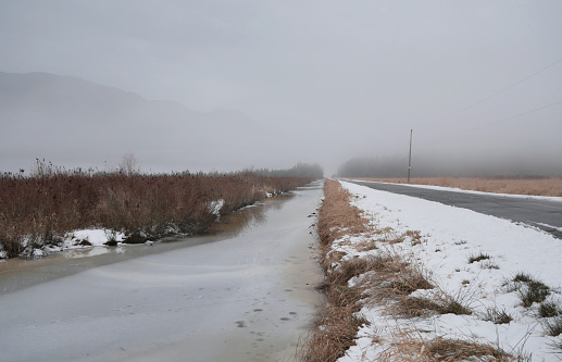 Looking down a ditch along Rannie Road near the Grant Narrows Regional Park and Pitt River Dike during a snowy winter season in Pitt Meadows, British Columbia, Canada.