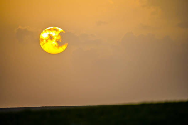 The sun, partially hidden behind clouds, creates a dramatic and fiery appearance as it sets on the horizon