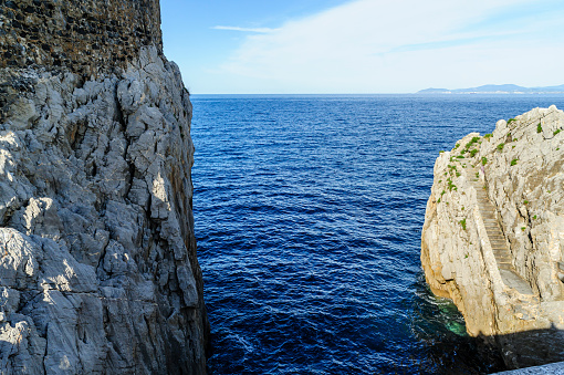 A natural limestone cliff majestically towers over the serene blue sea waters under a clear sky