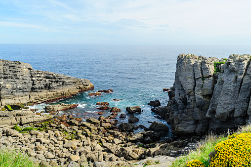 Striking layered rock formations along the rugged coast of Northern Spain with a clear blue sky overhead.