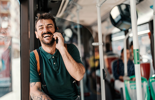 A happy trendy passenger is using public bus and talking on the phone.