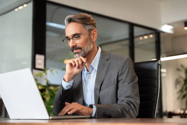Focused mature European business man ceo trader using computer. Businessman typing, working in modern office, doing online data market analysis, thinking planning tech strategy at laptop, closeup.