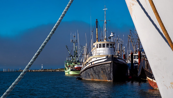 Fishing boat tied down in harbor is seen through view from another vessel and anchor rope