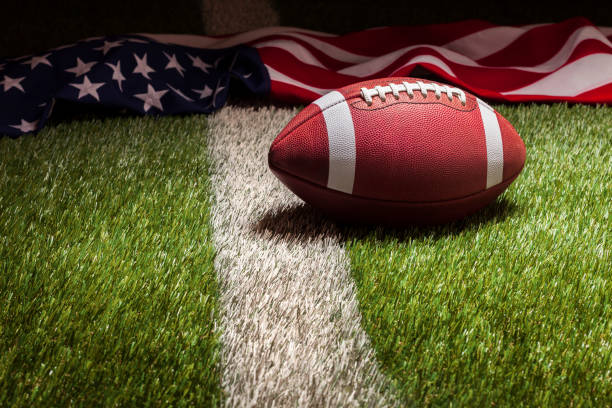 istock Football and American flag on grass field with stripe in dramatic light 1965572069