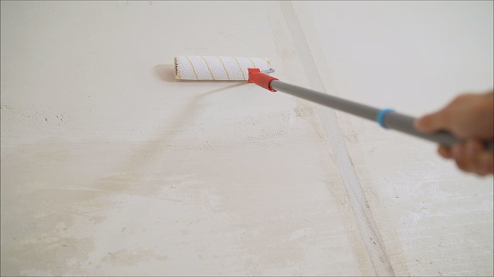 Primer worker with paint roller. white primer painting with roller brush on the repair cement wall construction background
