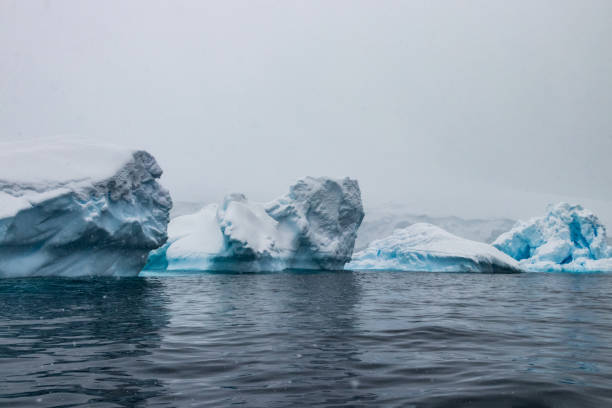 istock Blue ice, Antarctic Peninsula coastline. Gray sky with snow falling, dark blue water. 1965640027