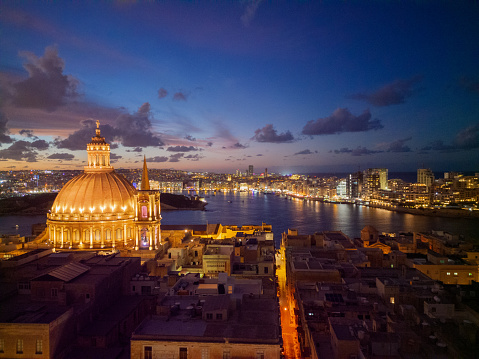 Beautiful illuminated dome of Basilica of Our Lady of Mount Carmel in Valletta. Aerial view with bright orange street line towards Sliema skyline and light reflection on the sea.