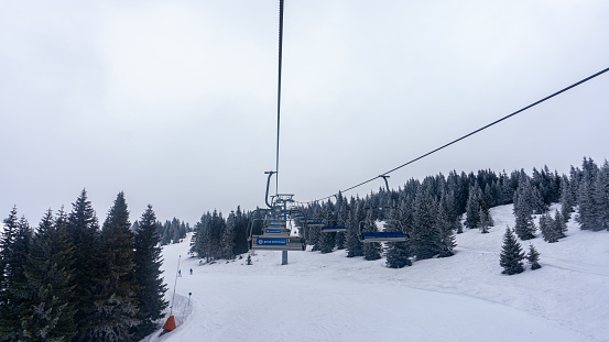Kopaonik, Serbia-26 March, 2019: Cold winter scenery on a grey cloudy day with a cable car leading all the way to the top of a mountain for skiing and other winter sports. Adventure and activities on the snow during winter time on the mountain. Ski slopes and trees covered with white snow.
