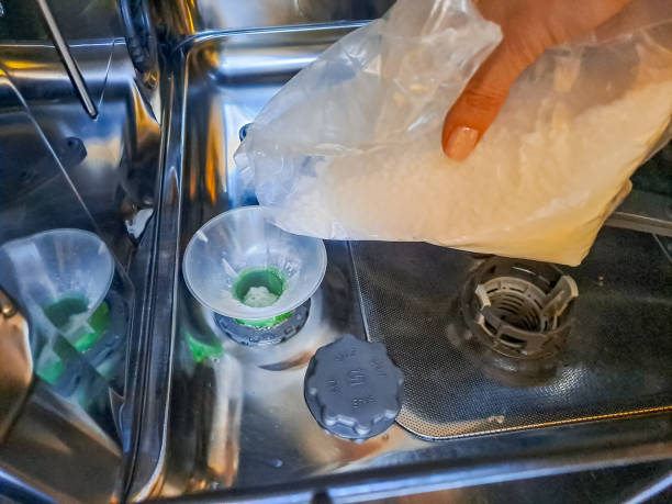 a woman who gradually pours sea salt into the dishwasher. - water softener stock-fotos und bilder