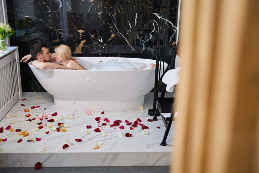 Young couple enjoying a warm bubble bath, the floor is decorated with rose petals