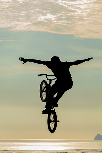 Freestyle cyclist practicing street BMX in backlight at sunset