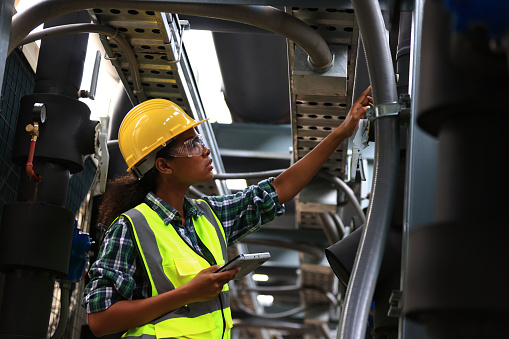 Female engineer wearing a yellow safety vest and yellow helmet  working check Industry cooling system, HVAC of large industrial building
