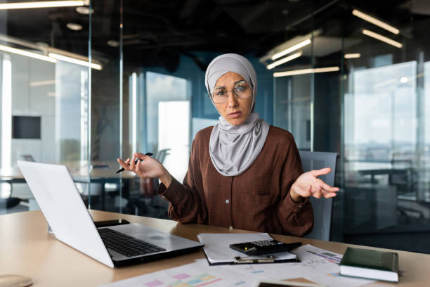 istock Financial problems in the workplace. Young Muslim woman works in the office with a notebook and documents, looks upset at the camera, throws her hands in frustration 1965728822