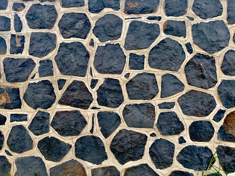 Horizontal closeup photo of a decorative stone feature wall made from large pieces of dark grey granite cemented together. Uralla, New England high country NSW.