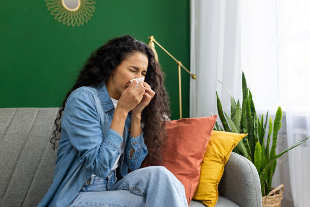 istock Young woman feeling unwell with cold or flu symptoms, sneezing into tissue on cozy home sofa, indoor wellness concept 1965780983