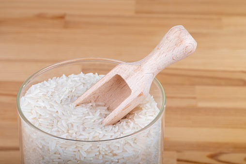 Glass storage jar full of rice with a wooden spoon on a table