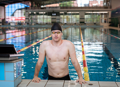 Portrait of a young professional athlete, a swimmer with a black swimming cap looking at the camera with goggles