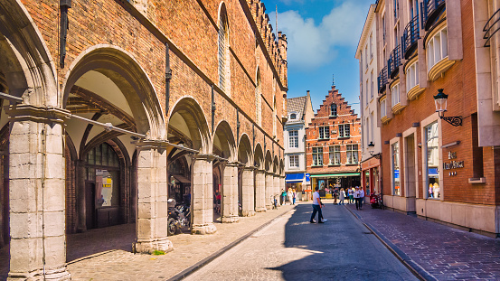 Bruges,Belgium-June 3, 2023 - Tourists and shoppers  stroll along the sidewalks and narrow streets of Bruges where modern hotel architecture on the right blends seamlessly with the ancient structures along the street.