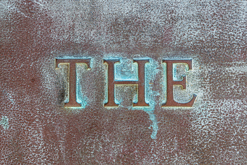 THE: Lettering THE on a bronze plate. Close-up of definite article THE on a bronze slab with oxidized green patina. Inscription on a bronze monument