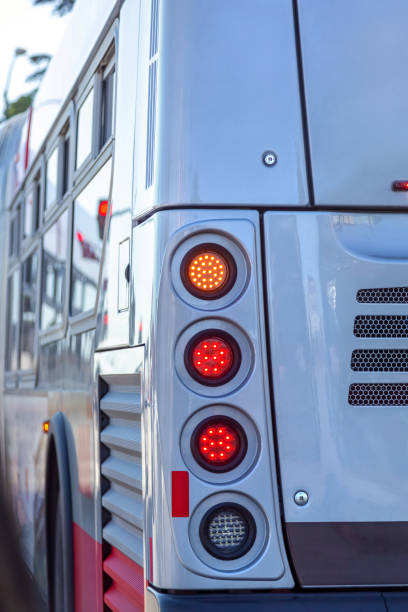 Close-up of rear glowing brake lights of a city bus standing at a traffic light. Rear lights on white bus. Close up, city bus tail light on city street.