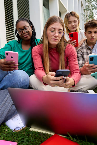 group of young multiracial university students immersed on their mobile cell technology addicted - multi ethnic group concentration mobile phone using laptop imagens e fotografias de stock