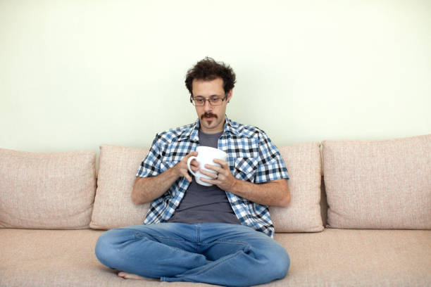 Young man sitting in sofa drinking coffee stock photo
