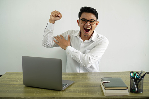 young asian businessman in a workplace doing strong gesture, wearing white shirt with glasses isolated