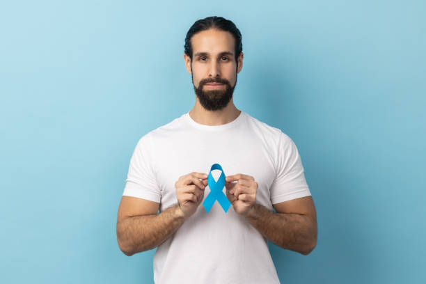 istock Man wearing white T-shirt holding blue awareness, disease symbol, looking at camera, support. 1966117731