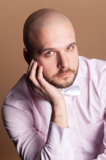 istock Calm serious attractive bald bearded man sitting keeps hand on his face, looking at camera. 1966120877