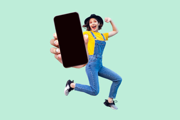 istock Happy surprised girl jumping and looking at camera, showing big empty smart phone display. 1966123027