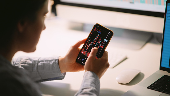 Woman studying stock markets on TradingView app, checking on trading positions and stock markets in the evening at home.