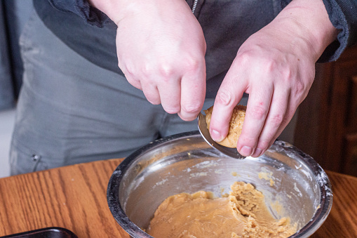 A person is using a silver spoon to scoop peanut butter cookie dough out of a metal mixing bowl.