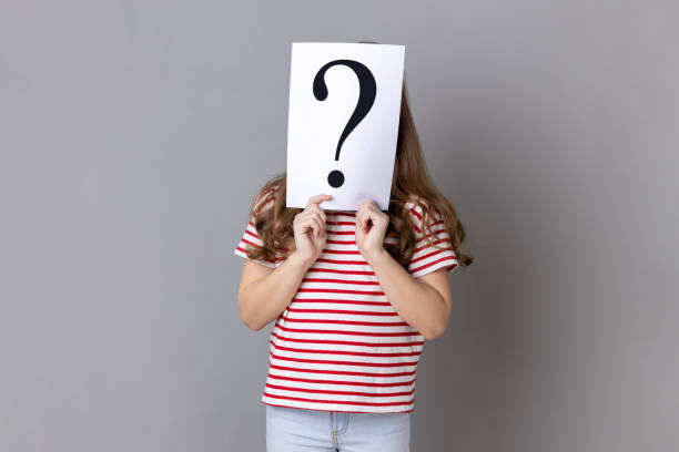 unknown little girl wearing striped t-shirt standing hiding face behind paper with question mark. - pensive question mark teenager adversity imagens e fotografias de stock