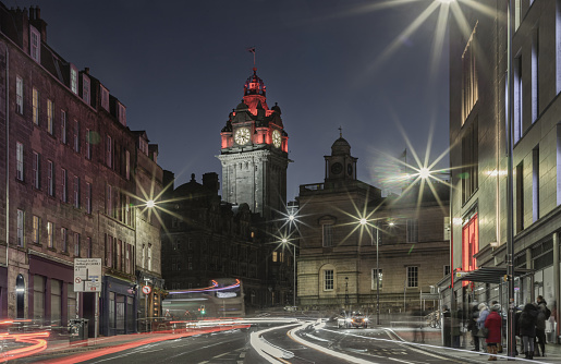 Edinburgh, Scotland - Jan 17, 2024 - A night-time view of Princes Street with Lights streak from vehicles and blurred people and The historic Balmoral hotel on background in Edinburgh. Scotland, United Kingdom, Space for text, Selective focus.