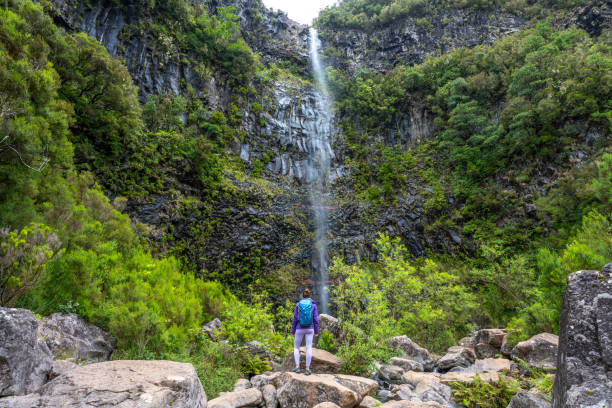 istock Female tourist with backpack enjoys atmosphere at waterfall falling from high rock wall. Lagoa do Vento waterfall, Madeira Island, Portugal, Europe. 1966340889