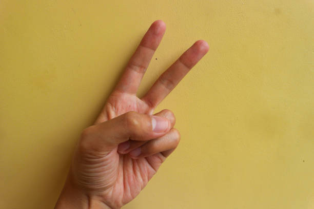 symbole gestów: cyfra dwa, symbol pokoju lub zwycięstwa na żółtym tle - cyfra_  zdjęcia i obrazy z banku zdjęć