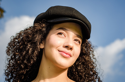 beautiful young white woman with curly hair and beret on blue sky background