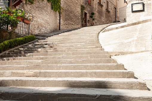 Wide concrete steps leading upward to arched entrance and turning left concrete steps rising and turning right in Gubbio, Italy.