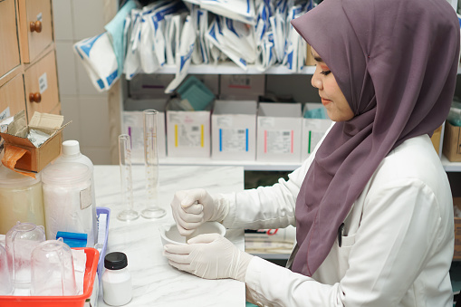 Indonesian Muslim women pharmacist wearing hijab mixing medicine in hospital