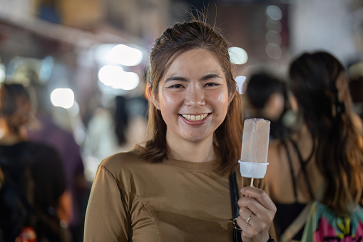 Happy young beautiful woman eating a traditional thai ice cream in the street food.