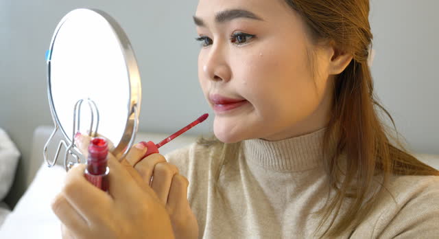 Young women using the mirror to apply her red lipstick getting ready to go to outside.