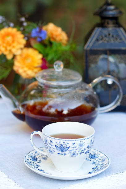 istock Patio table with cup of tea, pot, flowers and lantern. 1966651640
