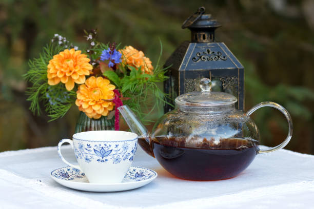 istock Patio table with cup of tea, pot, flowers and lantern. 1966651642